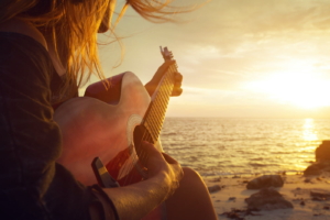 Young woman playing guitar on sunset beach.