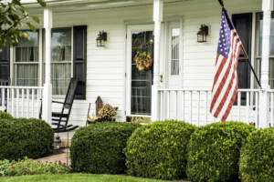 White colonial home decorated for fall with American flag flying from the front porch.