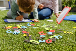 Colored letters in the garden while children write on their blackboards in the background.