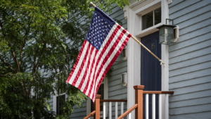 American flag in front of a building with tree in the background.