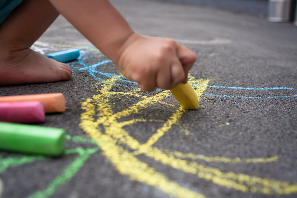 kid on playground plays with colored chalk