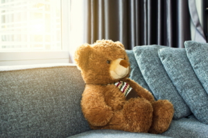 A teddy bear on gray sofa in living room with sunlight from the window