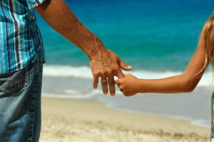 The parent holds the child's hand on the beach in summer
