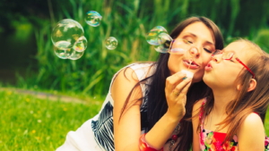 Mother and little girl daughter child blowing soap bubbles outdoor. Parent and kid having fun in park. Happy and carefree childhood. Good family relations.