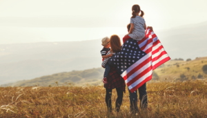 Happy family with US flag at sunset outdoors.