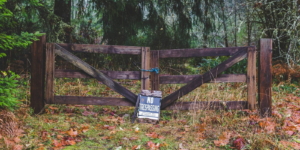 Wooden gate in rainy forest area with "No Trespassing" sign.
