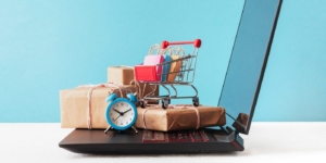 E-commerce sale and delivery service concept: shopping cart multicolored packages and boxes with trolleybus logo on laptop keyboard, blue background