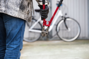 Man with bolt cutters walking towards a chained bike.