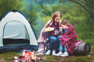 Family mother and child daughter drinking tea on a camping trip with a tent and by the bonfire