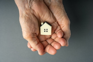 Inheritance concept. Elderly woman hands holds a little toy house. Inherited property idea.