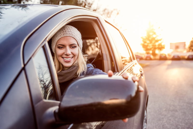 young blonde woman driving her car while smiling.