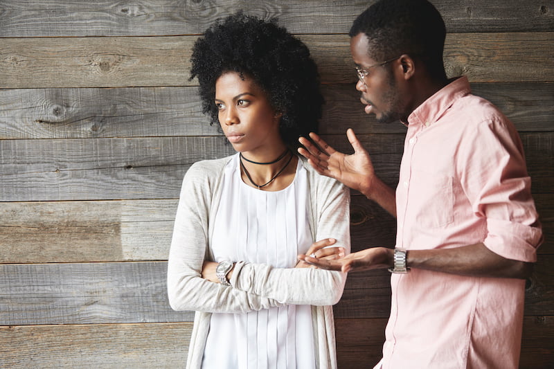 young black couple arguing, wood wall in background.