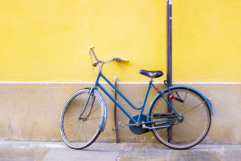 blue old bicycle standing near bright yellow wall.