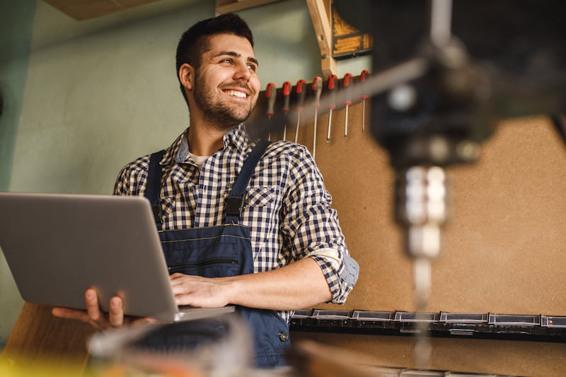 shot of a smiling carpenter using laptop at work in workshop.