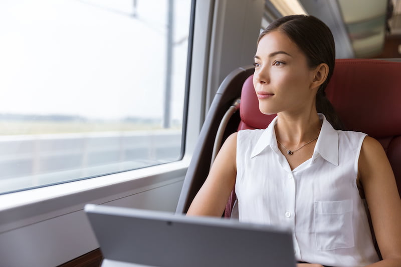 asian woman traveling using laptop in train. businesswoman pensive looking out the window while working on computer on travel commute to work.