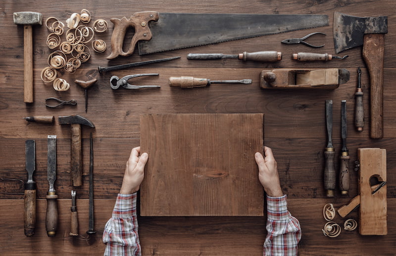 carpenter holding a wood block and collection of vintage woodworking tools on a workbench.