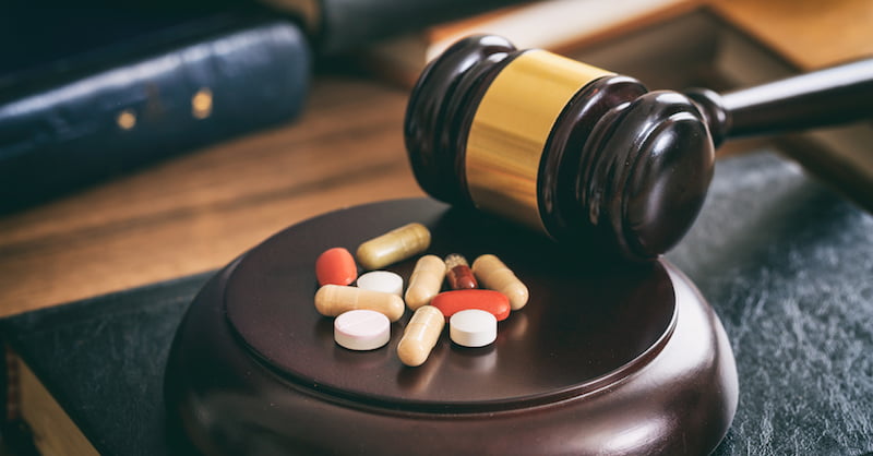 law gavel and colorful pills on a wooden desk, dark background