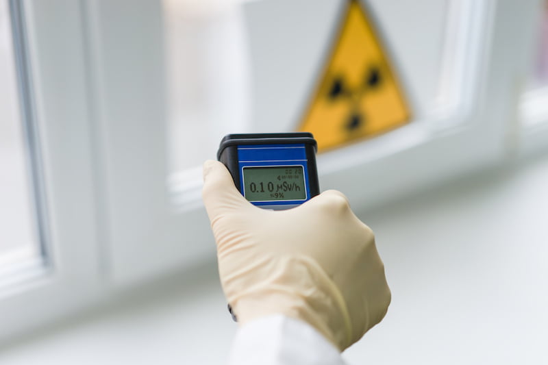 the scientist measures the level of radiation against the background of the sign of radiation hazard with the help of a dosimeter