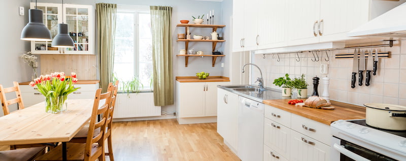 banner of a kitchen with kitchen table  and breakfast at the kitchen counter top white cupboards and wooden floor