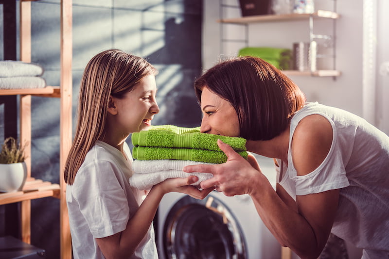 mother and daughter smelling fresh green towels at laundry room