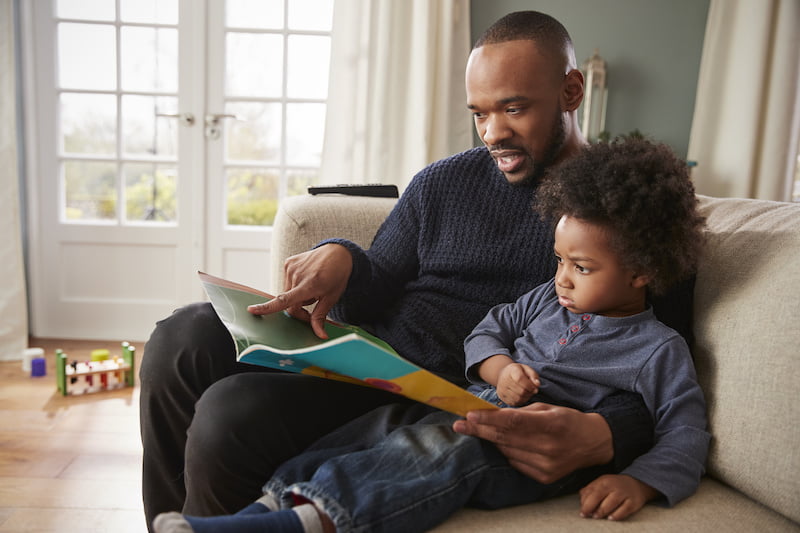 father and young son reading book together at home