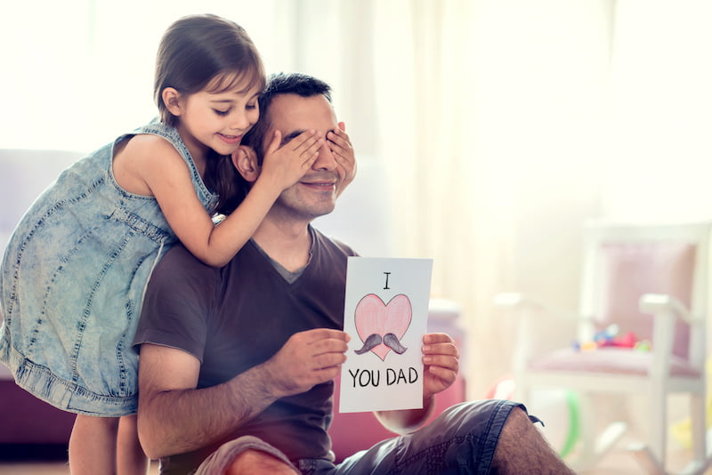 happy father's day concept. child daughter hiding surprise postcard present for her dad.
