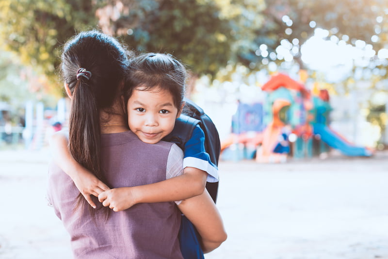 back to school. cute asian pupil girl with backpack hugging her mother in the playground