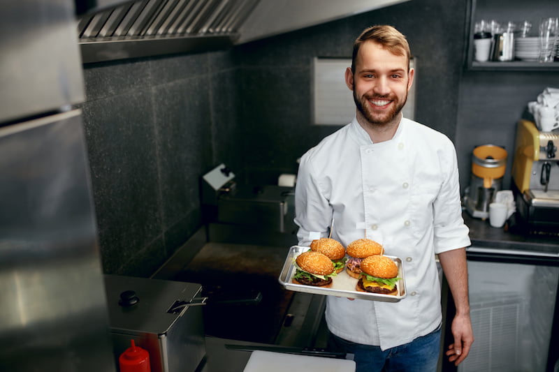 smiling chef with burgers in modern restaurant kitchen.