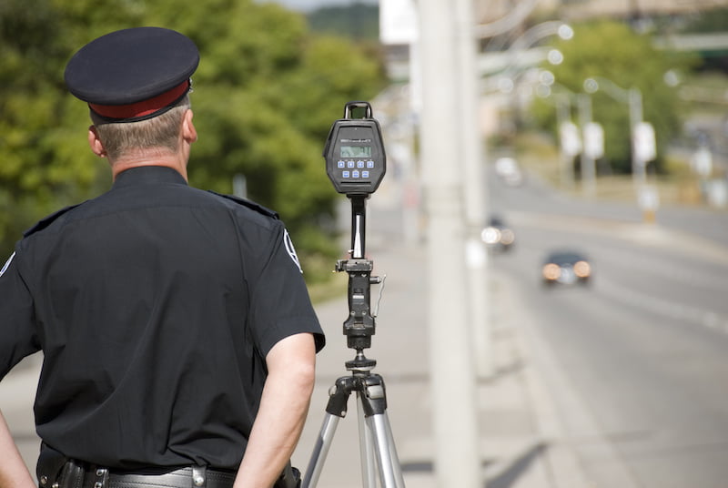 a north american policeman waits to catch speeding drivers with a radar gun. (shot with minimum depth of field. focus is on the police officer and radar gun.)