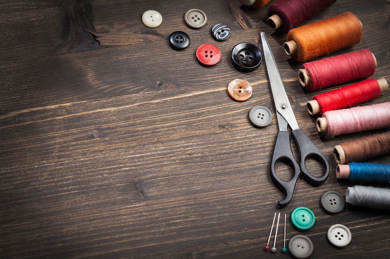scissors, bobbins with thread and needles on the old wooden background. vintage background
