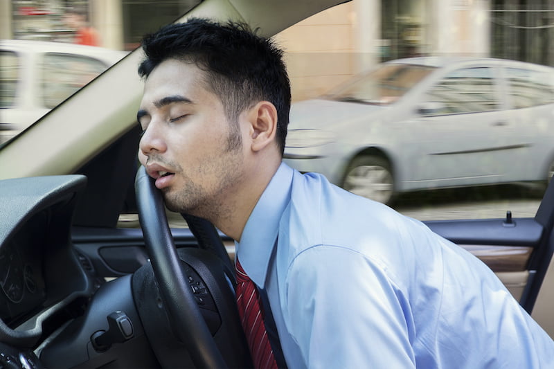 exhausted young businessman sleeping in the car while driving the car on the road