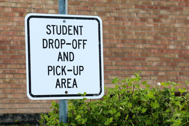 sign for student drop off and pick up area against brick school building