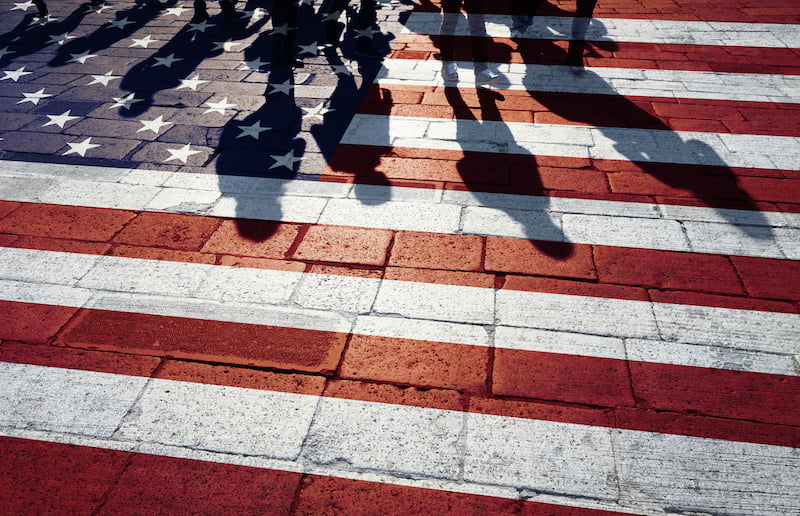 shadows of group of people walking through the streets with painted usa flag on the floor.