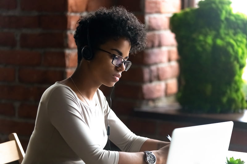 focused african american woman wearing headphones using laptop