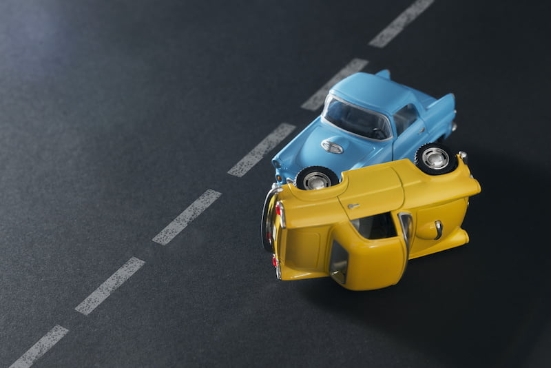 traffic accident by two toy cars blue and yellow on a black background with road lanes.