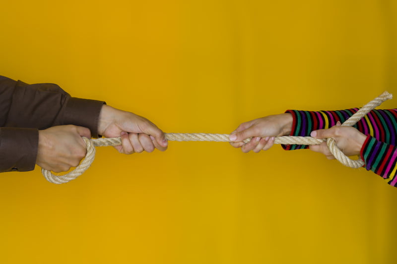 contested divorce concept, man and woman stretching a rope on yellow background.