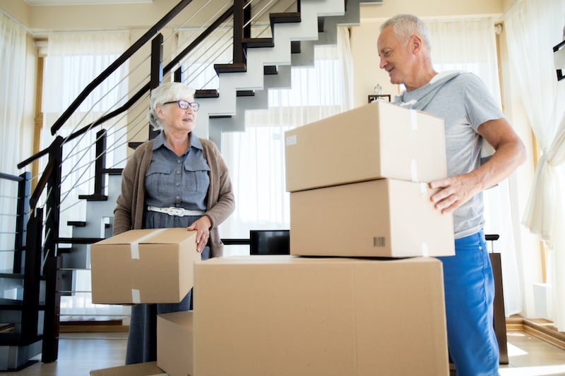 portrait of happy senior couple packing cardboard boxes while moving to new house