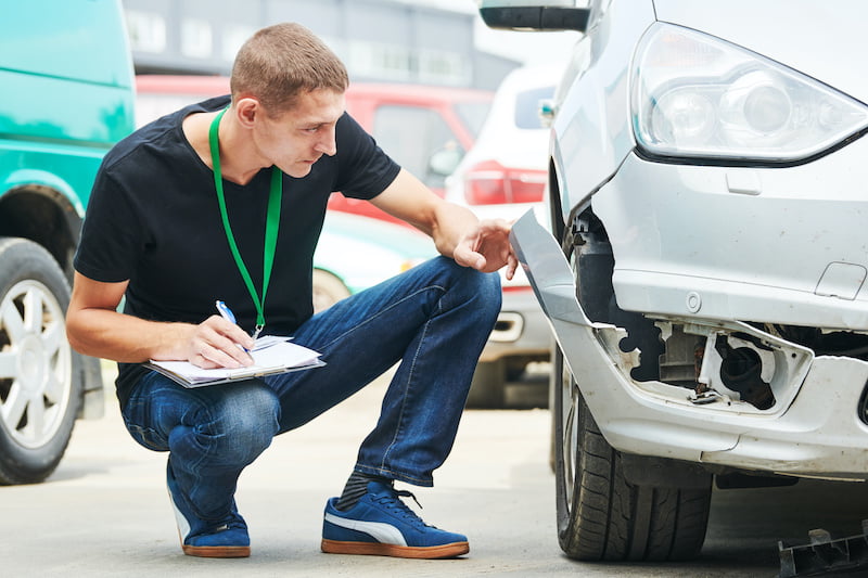 insurance agent recording damage after car crash during inspecting damaged automobile on claim form