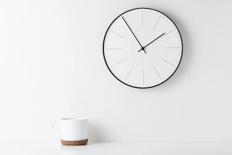 front view desk with round wall clock and cup on white background. home office minimal workspace desk