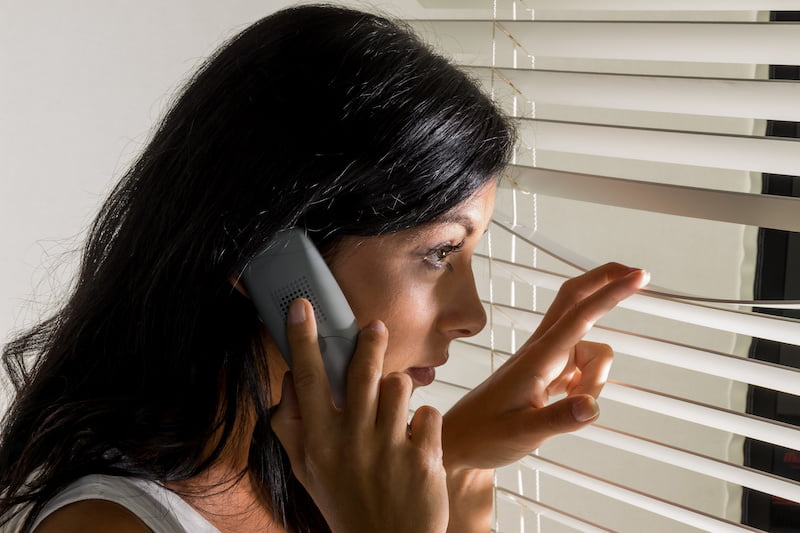 young woman looking out window while on phone, concerned.